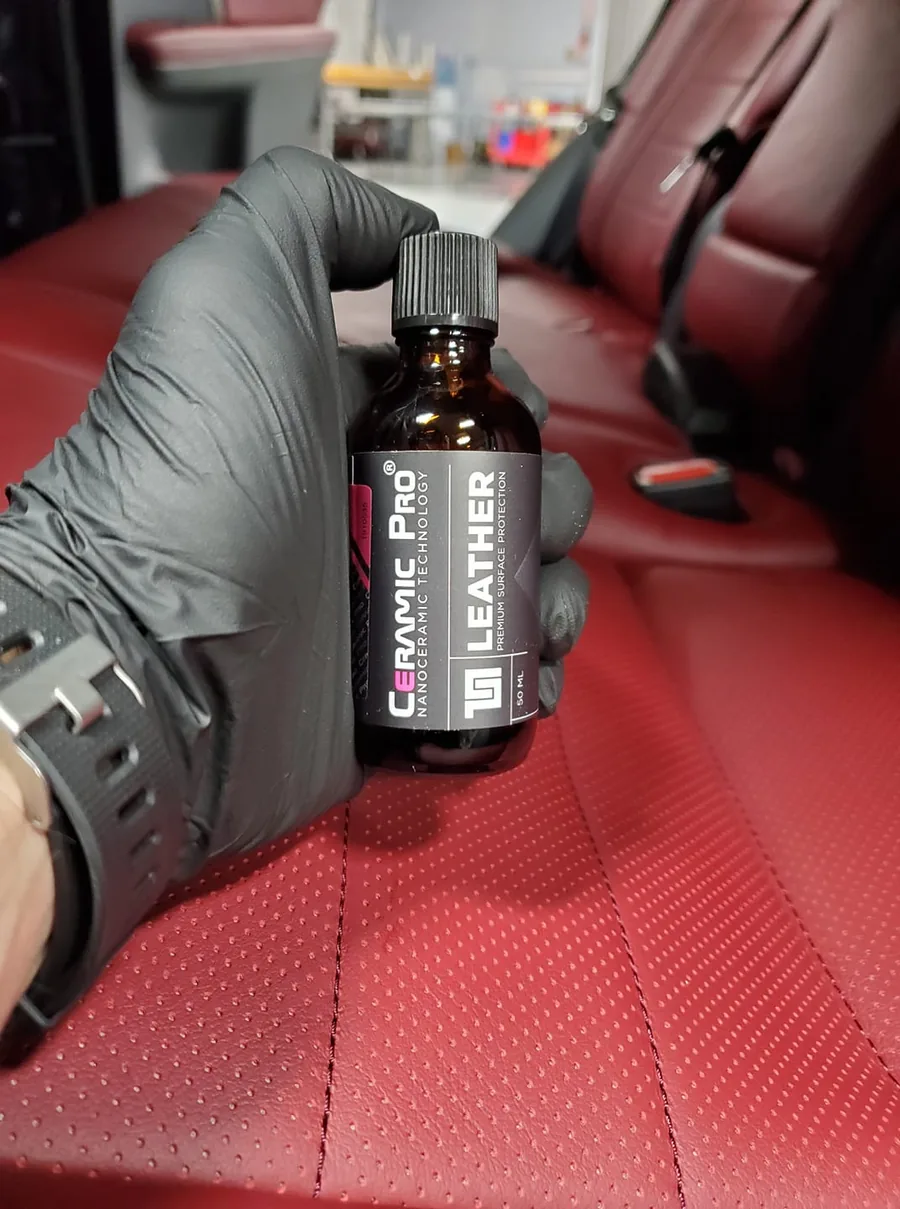 A gloved hand holding an interior leather coating bottle beside red leather seats