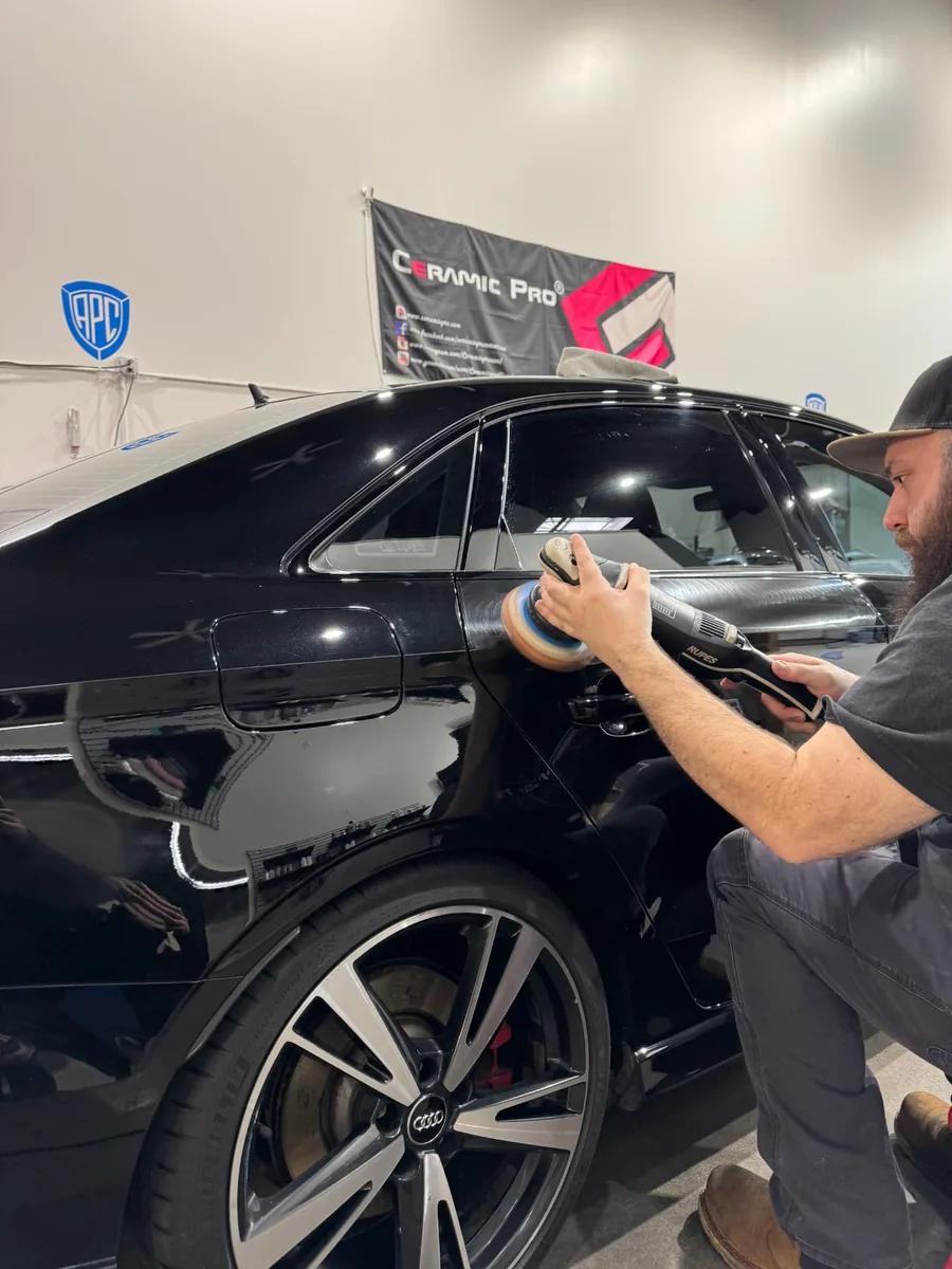 A technician machine-polishing the paint on a black Audi
