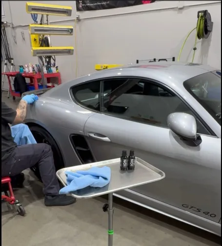 A technician applying ceramic coating to a silver Porsche inside the shop